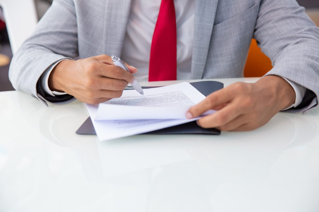 Cropped shot of businessman signing contract. Close-up partial view of African American businessman in formal wear working with papers in office. Paperwork concept